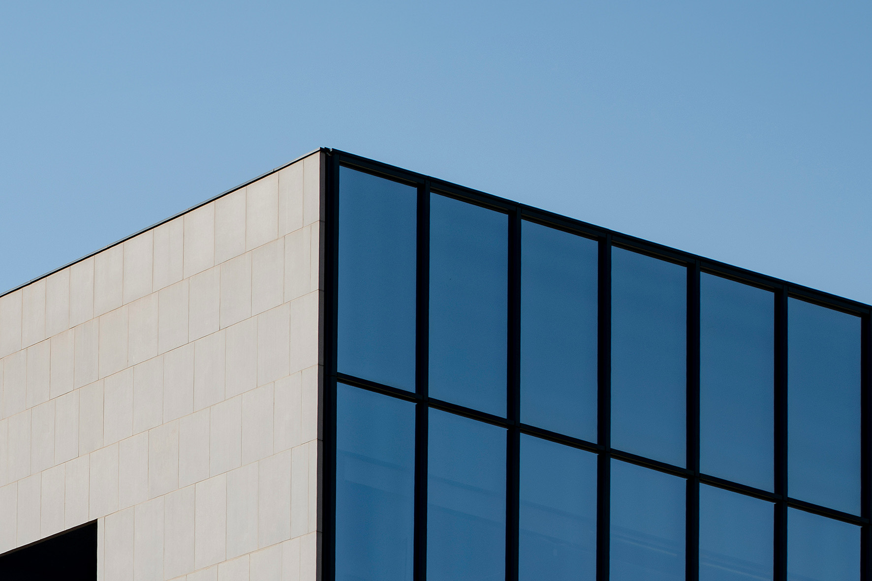 The corner of a stone and glass office building against a clear sky